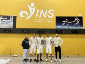 Une partie de l'équipe canadienne d'escrime posant sur le plateau d'escrime de l'INS Québec, devant un mur jaune.